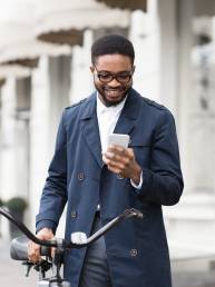 Way to work. Man texting on phone, standing with bike